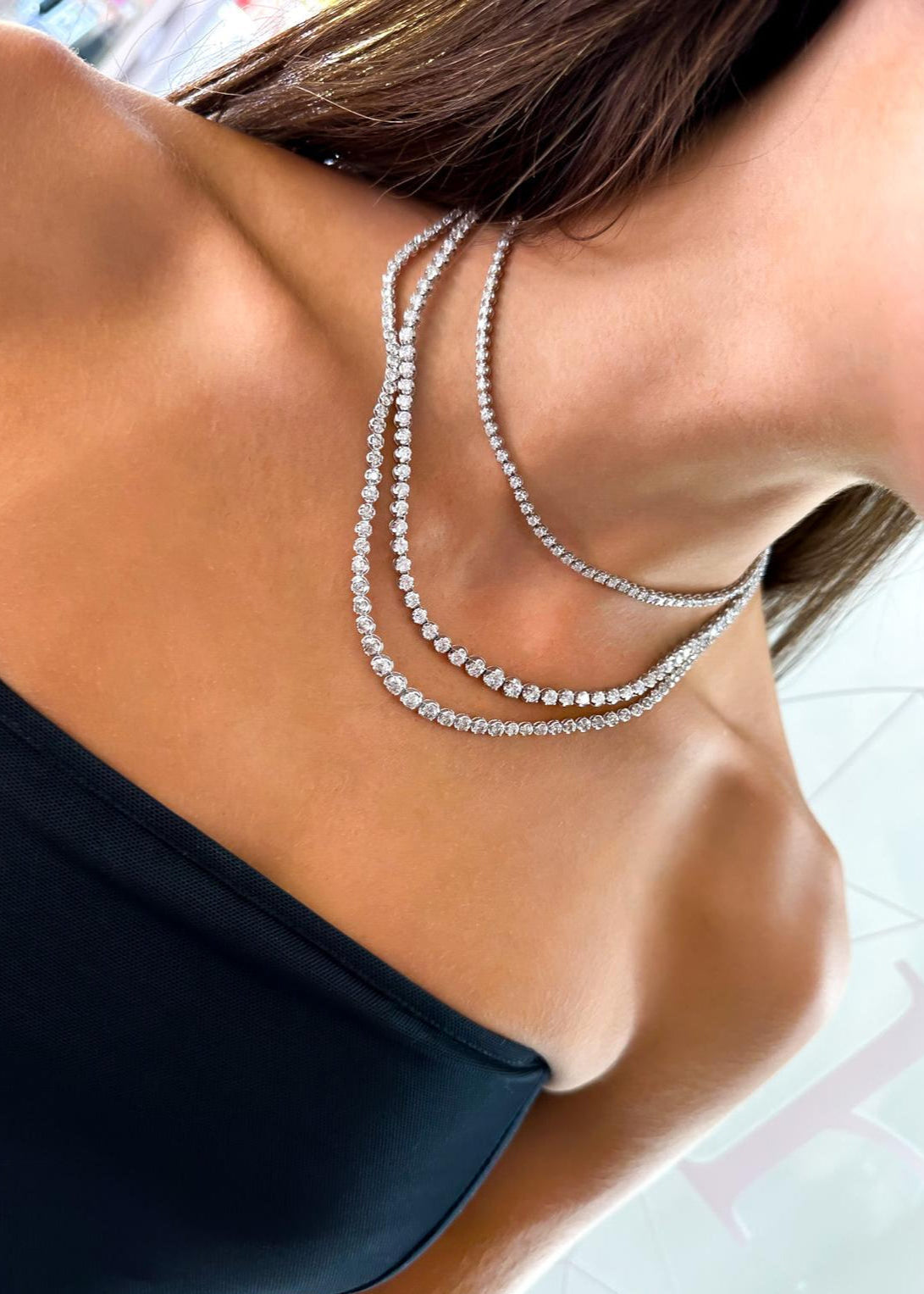 Close-up of a woman wearing a black top and multiple diamond necklaces.